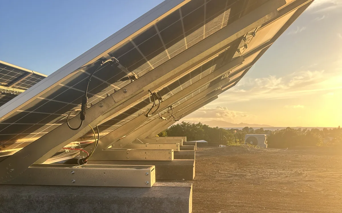 Rangees de panneaux solaires sur plots beton en toiture terrasse en Guadeloupe, au coucher du soleil